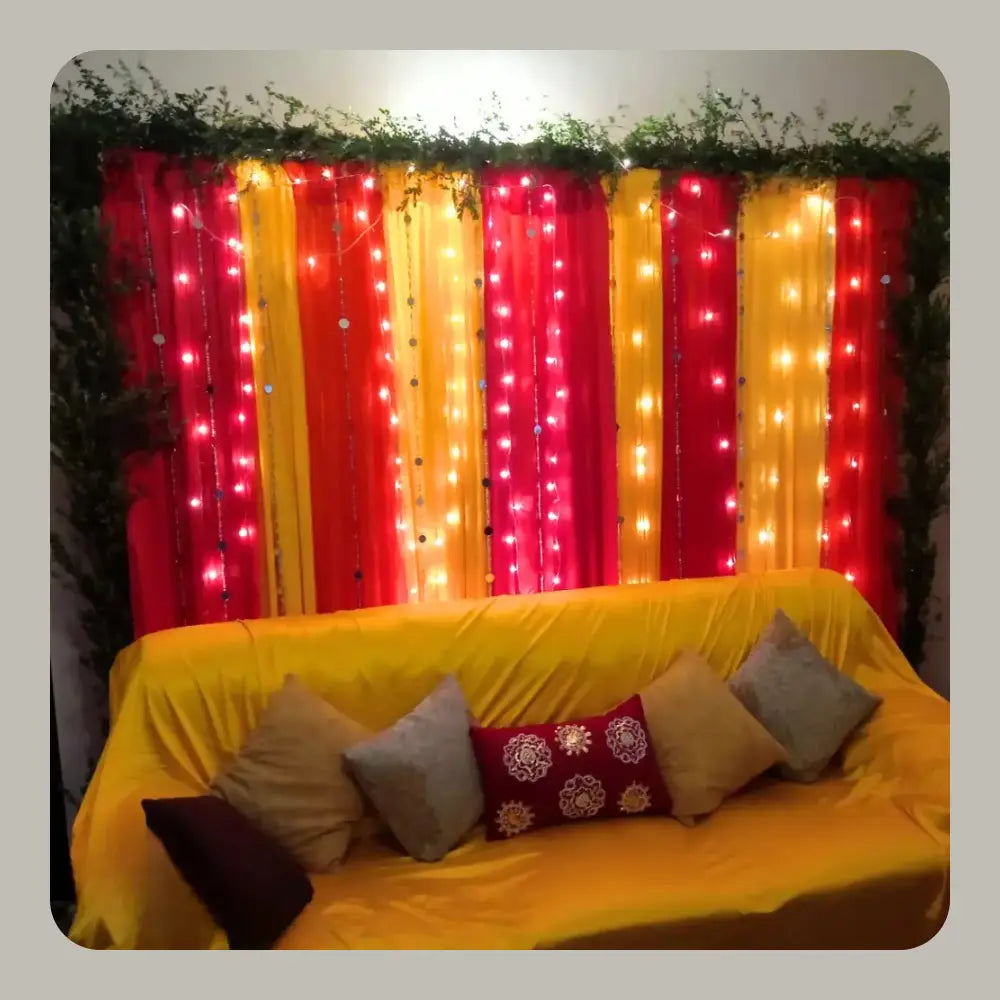 Vibrant Red and Yellow Mehndi Backdrop with Fairy Lights and Greenery Border